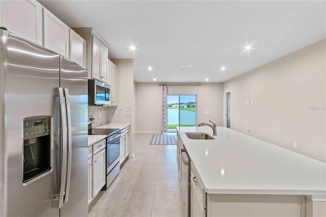 kitchen with light countertops, appliances with stainless steel finishes, a sink, and a kitchen island with sink