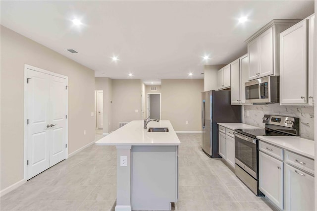 kitchen with stainless steel appliances, a sink, visible vents, tasteful backsplash, and an island with sink