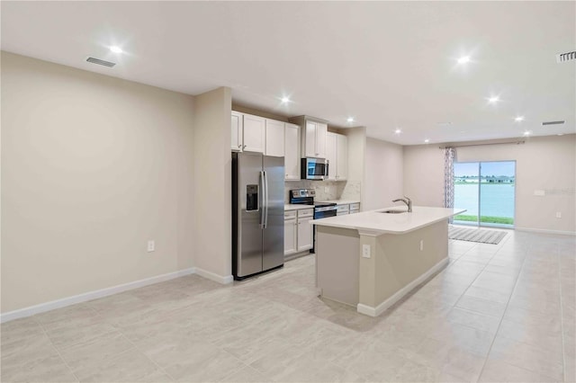 kitchen with stainless steel appliances, visible vents, light countertops, tasteful backsplash, and an island with sink