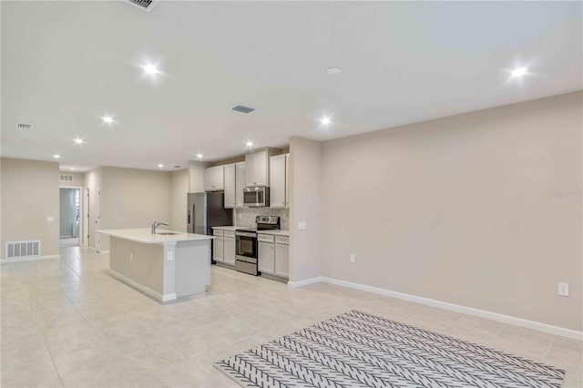 kitchen featuring visible vents, an island with sink, stainless steel appliances, light countertops, and a sink