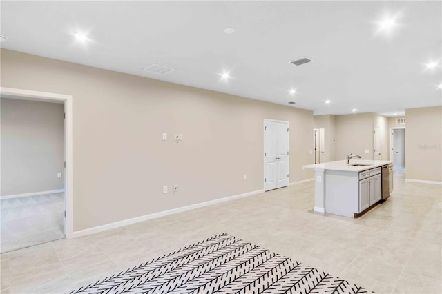 kitchen with baseboards, a sink, a kitchen island with sink, light countertops, and stainless steel dishwasher