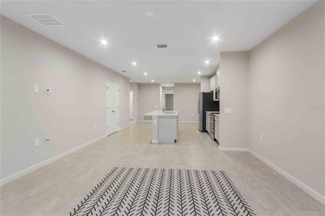 kitchen with a kitchen island with sink, a sink, visible vents, white cabinetry, and light countertops