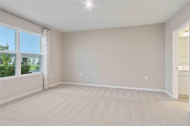 spare room featuring light carpet, a sink, and baseboards