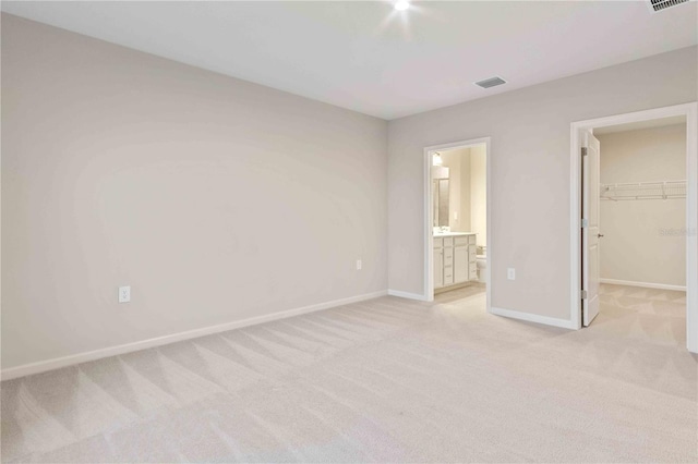 unfurnished bedroom featuring light colored carpet, a walk in closet, visible vents, and baseboards