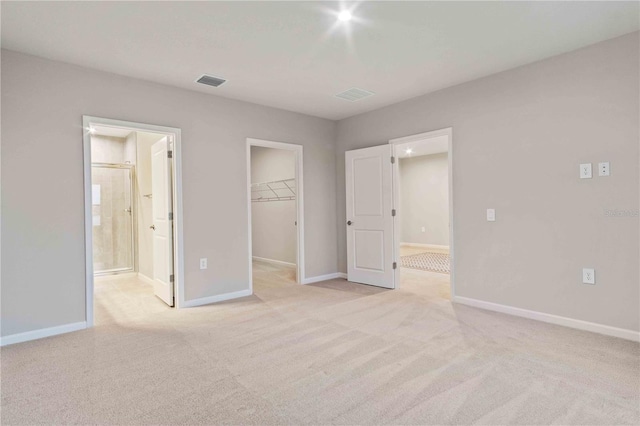 unfurnished bedroom with light colored carpet, visible vents, baseboards, a closet, and a walk in closet