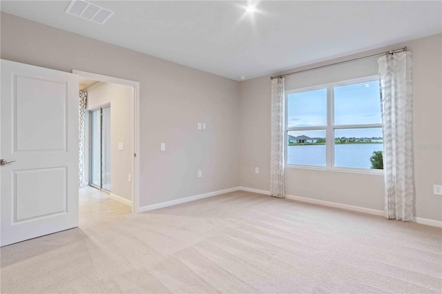 unfurnished room featuring light colored carpet, visible vents, a water view, and baseboards