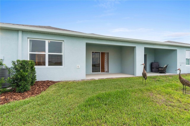 rear view of property featuring a patio, a yard, central AC unit, and stucco siding