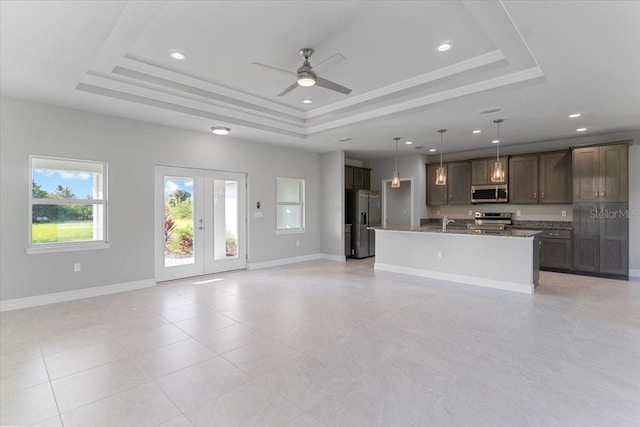 kitchen with stone counters, a kitchen island with sink, appliances with stainless steel finishes, and a tray ceiling