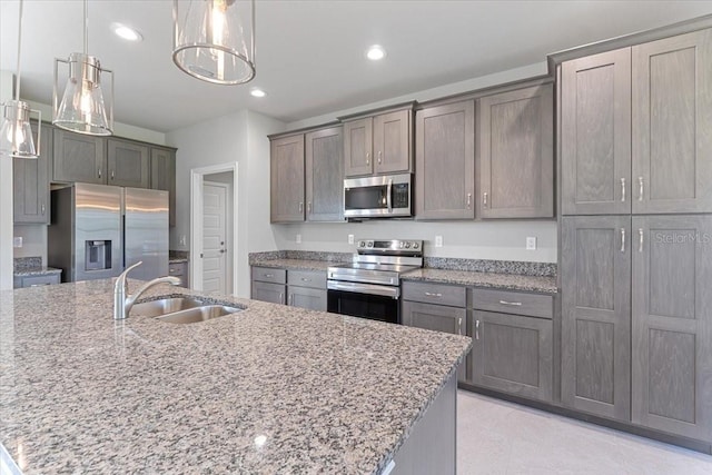 kitchen with hanging light fixtures, appliances with stainless steel finishes, sink, and a center island with sink