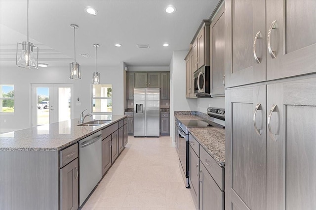 kitchen featuring a spacious island, stainless steel appliances, sink, hanging light fixtures, and light stone counters