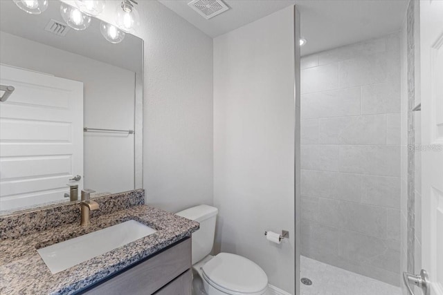 bathroom featuring toilet, vanity, and tiled shower