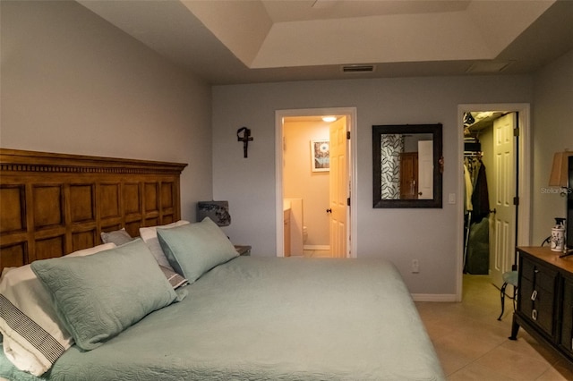 bedroom featuring a spacious closet, light tile patterned floors, a tray ceiling, and connected bathroom