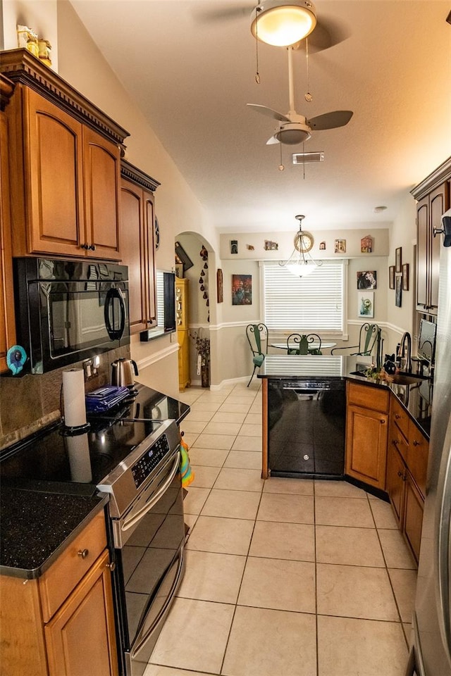 kitchen with black appliances, kitchen peninsula, ceiling fan, dark stone countertops, and light tile patterned floors