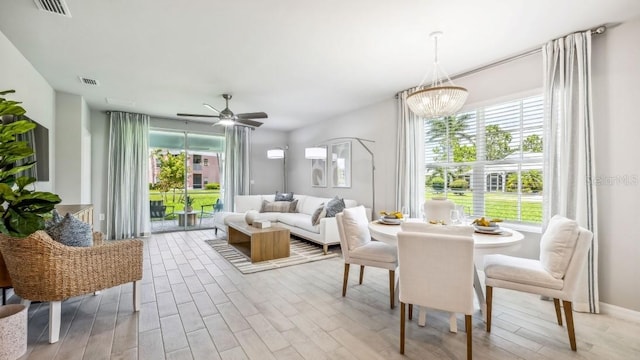 dining space with ceiling fan with notable chandelier and light hardwood / wood-style flooring