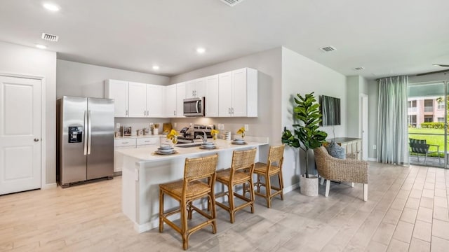 kitchen with stainless steel appliances, white cabinetry, light hardwood / wood-style floors, a breakfast bar, and kitchen peninsula