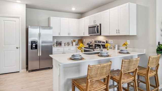 kitchen with white cabinetry, stainless steel appliances, a kitchen bar, and kitchen peninsula