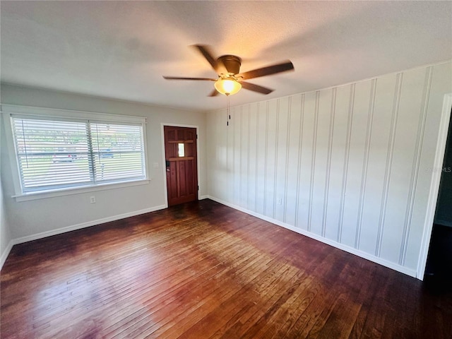 empty room with ceiling fan, dark wood finished floors, and baseboards