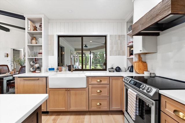 kitchen with stainless steel electric stove, sink, custom exhaust hood, and light wood-type flooring