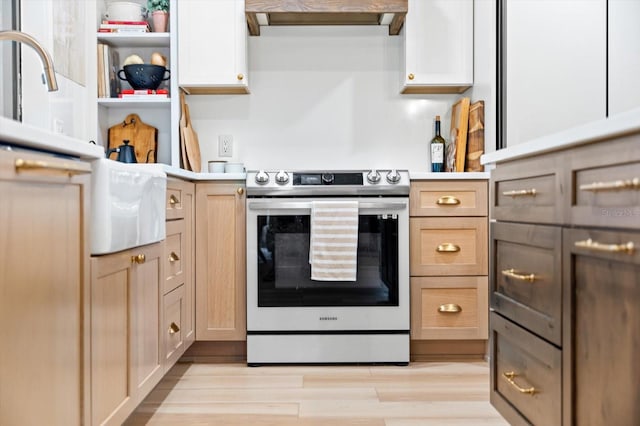 kitchen featuring stainless steel electric range, exhaust hood, white cabinets, and light brown cabinets