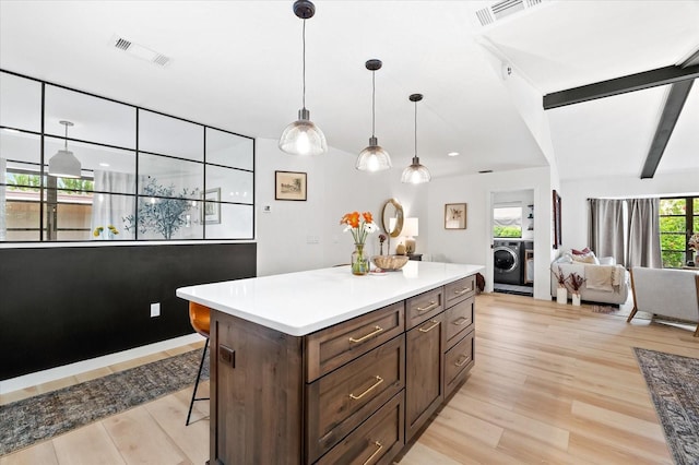 kitchen with a kitchen bar, washer / dryer, light hardwood / wood-style floors, and hanging light fixtures