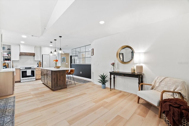 kitchen with hanging light fixtures, stainless steel electric range, light wood-type flooring, and a kitchen island