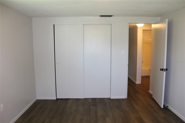 unfurnished bedroom featuring a closet, a textured ceiling, and dark wood-type flooring