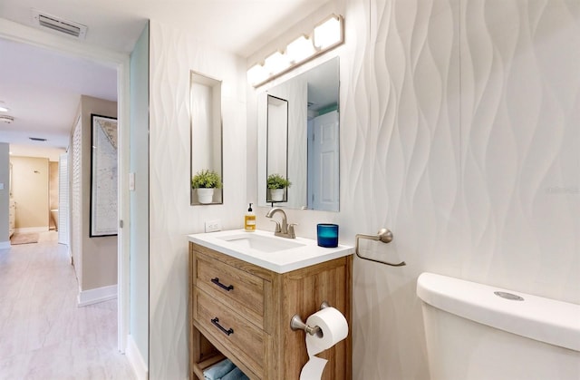 half bath with toilet, vanity, visible vents, and baseboards