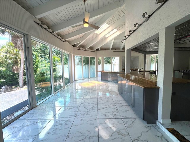 unfurnished sunroom with ceiling fan, sink, a healthy amount of sunlight, and vaulted ceiling with beams