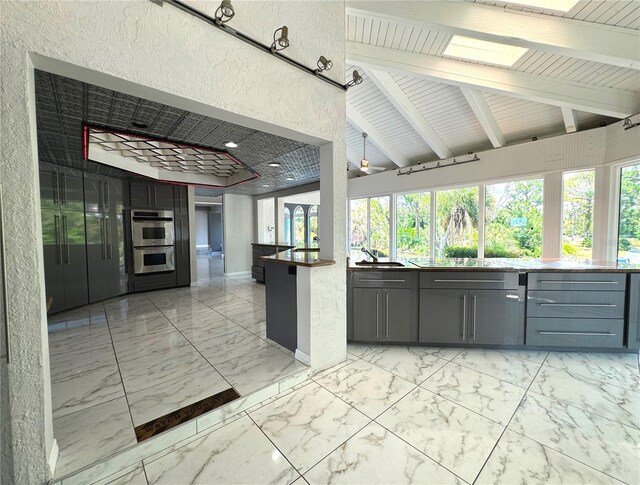 kitchen featuring gray cabinets, light tile patterned flooring, sink, double oven, and vaulted ceiling with beams