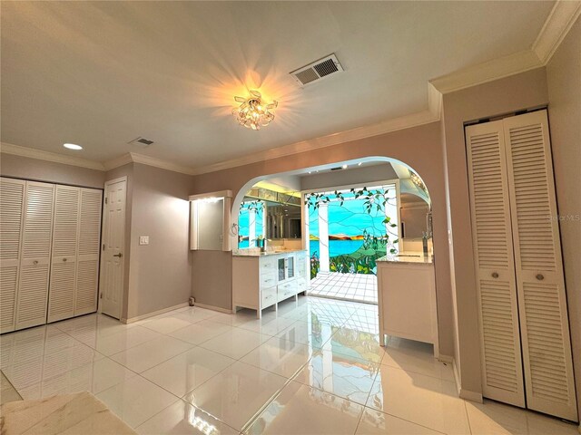 unfurnished bedroom with light tile patterned flooring, two closets, and crown molding