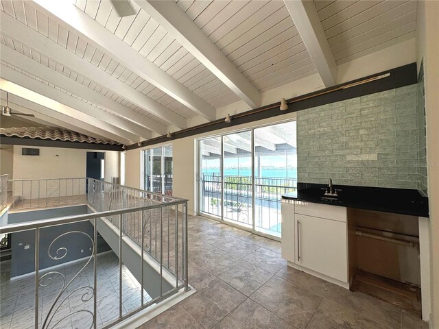 kitchen featuring lofted ceiling with beams, white cabinetry, tile walls, tile patterned floors, and sink