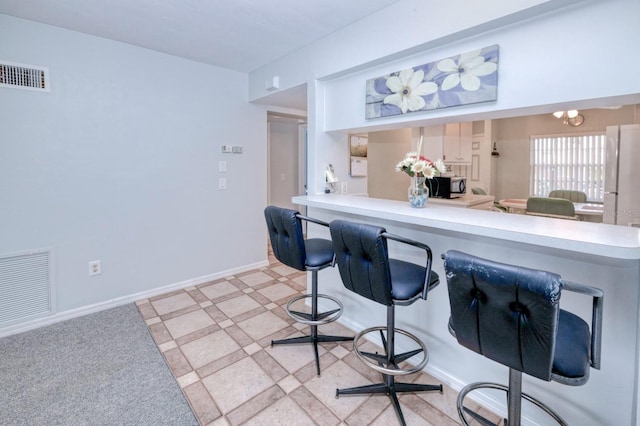 kitchen featuring a kitchen breakfast bar, light carpet, a chandelier, and kitchen peninsula