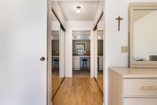 corridor with light wood-type flooring and a textured ceiling