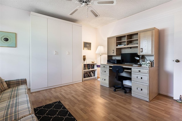 home office featuring ceiling fan, light wood-type flooring, a textured ceiling, and built in desk