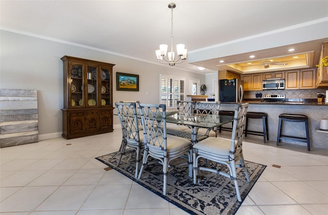 dining space featuring a tray ceiling, light tile patterned floors, a notable chandelier, and crown molding