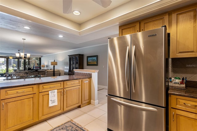 kitchen with light tile patterned flooring, tasteful backsplash, stainless steel refrigerator, dark stone counters, and ceiling fan with notable chandelier