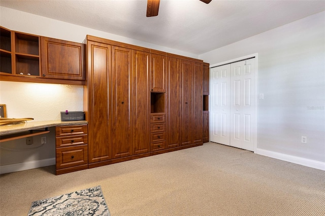 unfurnished office with built in desk, light colored carpet, and ceiling fan