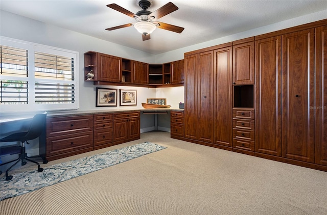 carpeted home office with built in desk and ceiling fan