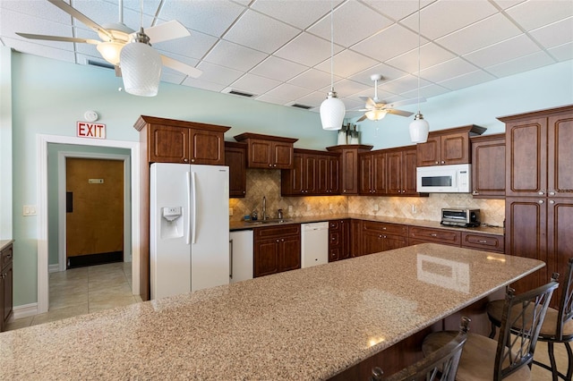 kitchen with sink, a breakfast bar area, white appliances, ceiling fan, and decorative backsplash