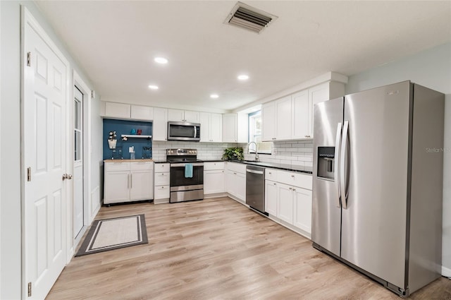 kitchen with white cabinetry, sink, appliances with stainless steel finishes, light hardwood / wood-style floors, and backsplash