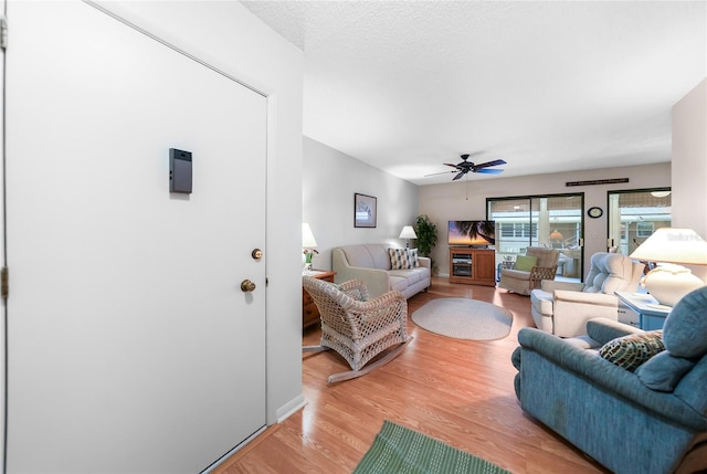 living area with ceiling fan, light wood-style flooring, and a textured ceiling