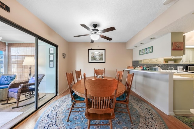 dining room featuring a textured ceiling, light wood-type flooring, sink, and ceiling fan