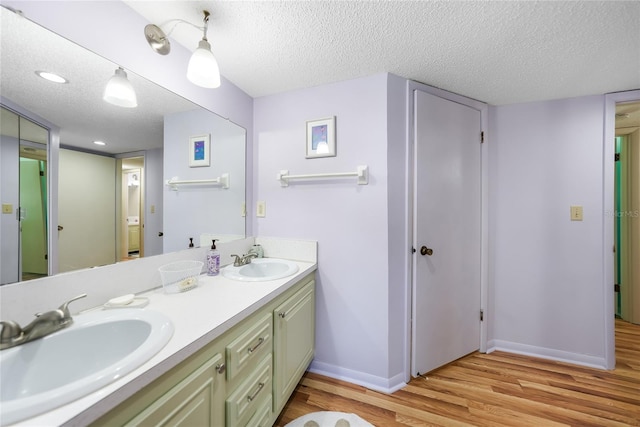 full bathroom with a sink, a textured ceiling, baseboards, and wood finished floors