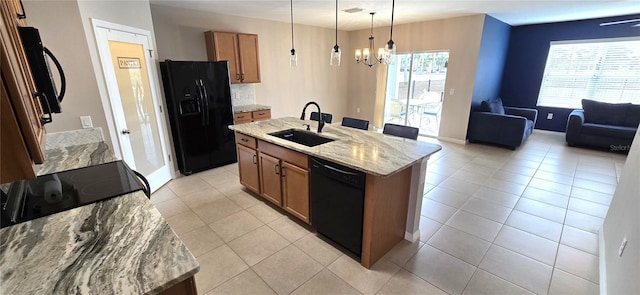 kitchen with light stone counters, a kitchen island with sink, sink, black appliances, and decorative light fixtures