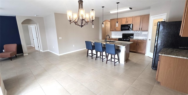 kitchen with tasteful backsplash, a breakfast bar, black appliances, a center island with sink, and hanging light fixtures