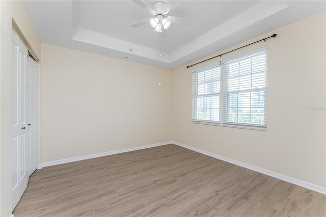 empty room with light wood-type flooring, ceiling fan, and a tray ceiling