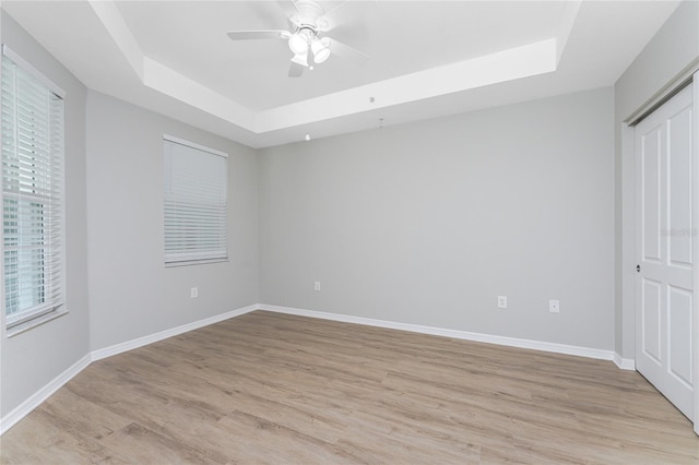 unfurnished bedroom featuring a tray ceiling, ceiling fan, and light wood-type flooring