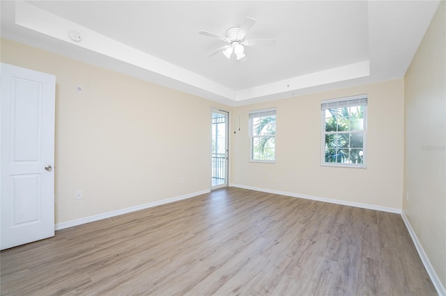 unfurnished room with light wood-type flooring, a raised ceiling, and ceiling fan