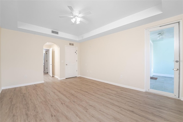 empty room featuring ceiling fan, a raised ceiling, and light hardwood / wood-style flooring