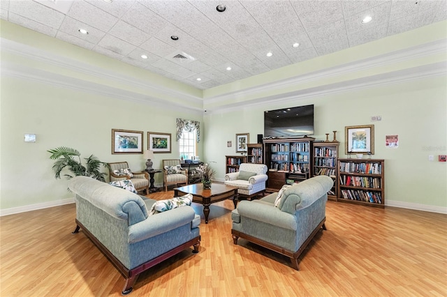 living room with light hardwood / wood-style flooring, a raised ceiling, and ornamental molding